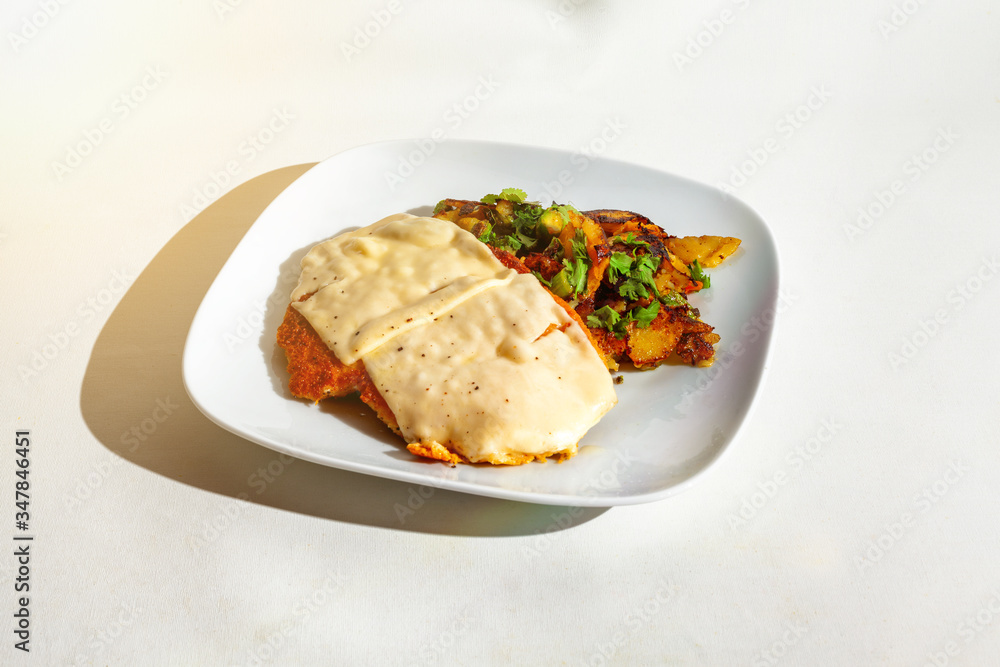 Schnitzel mit Käse überbacken mit Bratkartoffeln auf einen weißen Teller-Isoliert auf weiß