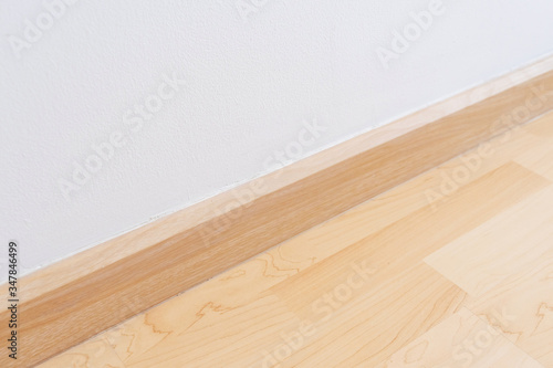 Wooden wall base skirting  finishing material with wood laminate floor and white mortar wall.