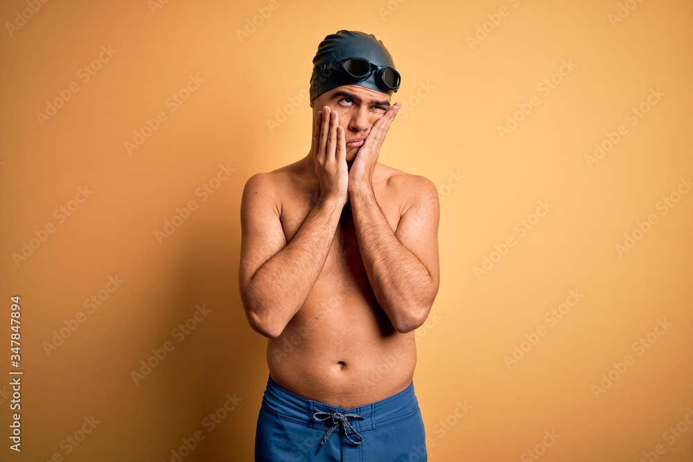 Young handsome man shirtless wearing swimsuit and swim cap over isolated yellow background Tired hands covering face, depression and sadness, upset and irritated for problem