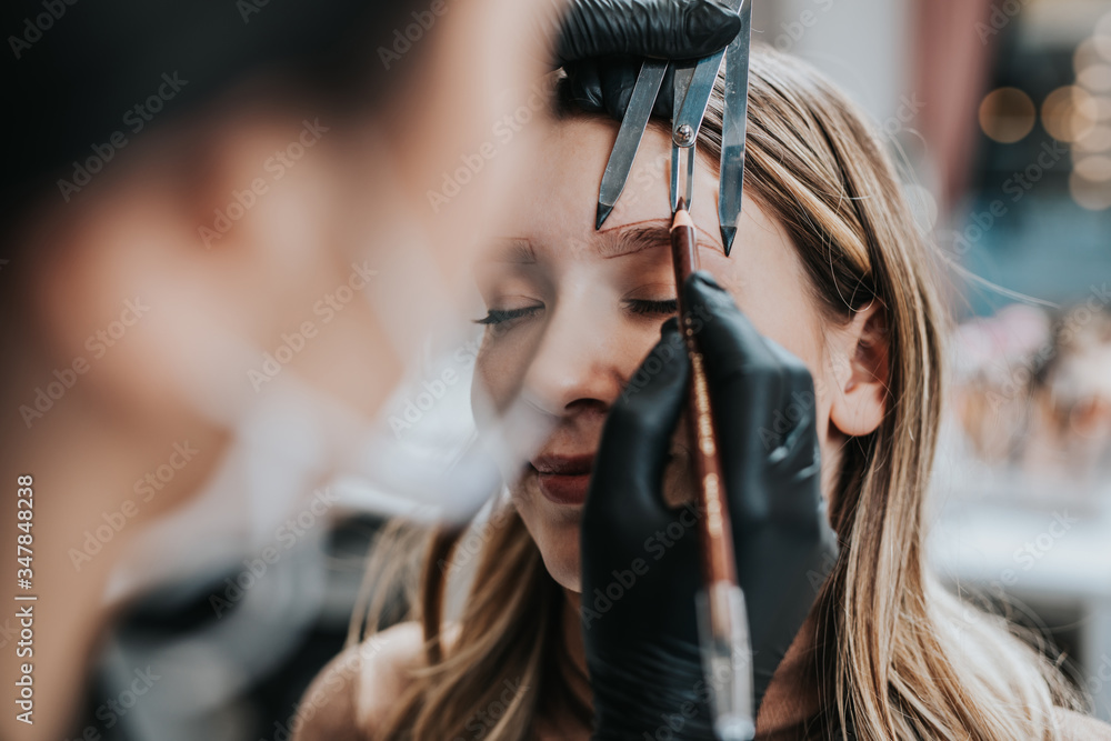 Cosmetologist measures the proportions of the eyebrows with the ruler. Micropigmentation work flow in a beauty salon.