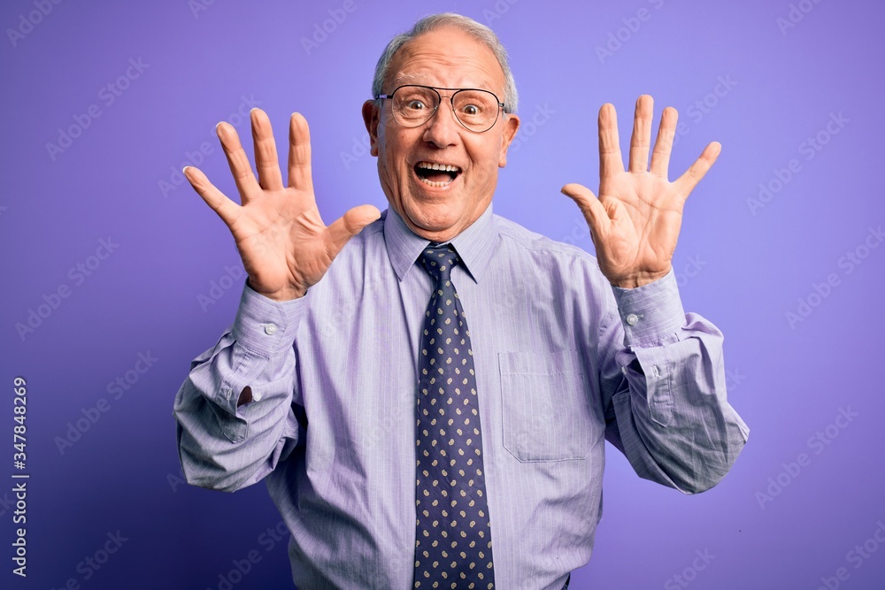 Grey haired senior business man wearing glasses standing over purple isolated background showing and pointing up with fingers number ten while smiling confident and happy. Grey haired senior business man wearing glasses standing over purple isolated background showing and pointing up with fingers number ten while smiling confident and happy.