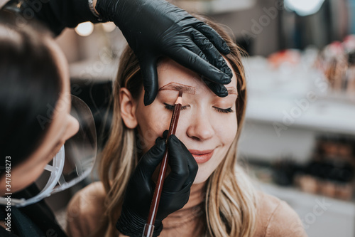 Eyebrows microblading concept. Cosmetologist preparing young woman for eyebrow permanent makeup procedure.