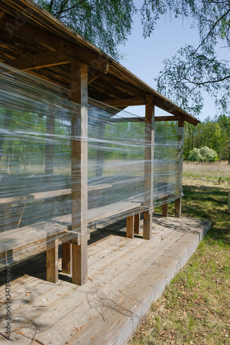 Wooden gazebo insulated with plastic film on the background of the forest in Ukraine. Vertical image.