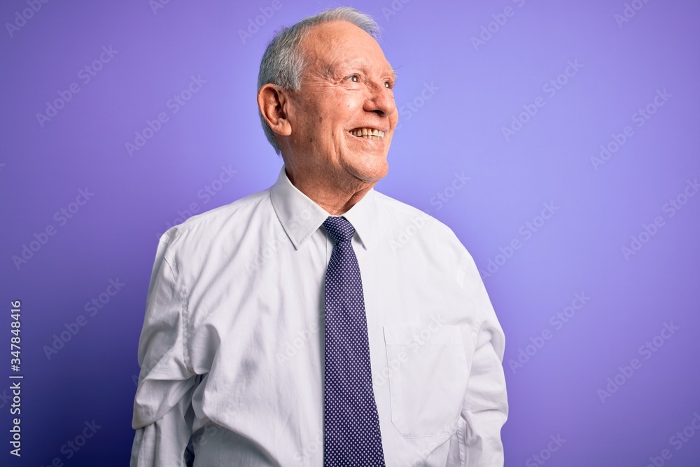 Grey haired senior business elegant man standing over purple isolated background looking away to side with smile on face, natural expression. Laughing confident. Grey haired senior business elegant man standing over purple isolated background looking away to side with smile on face, natural expression. Laughing confident.