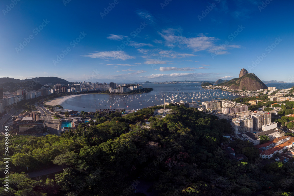 Botafogo beach and Sugarloaf mountain on either side of Guanabara bay port for pleasure boats against a blue sky with the Pasmado hill park and viewpoint in the foreground