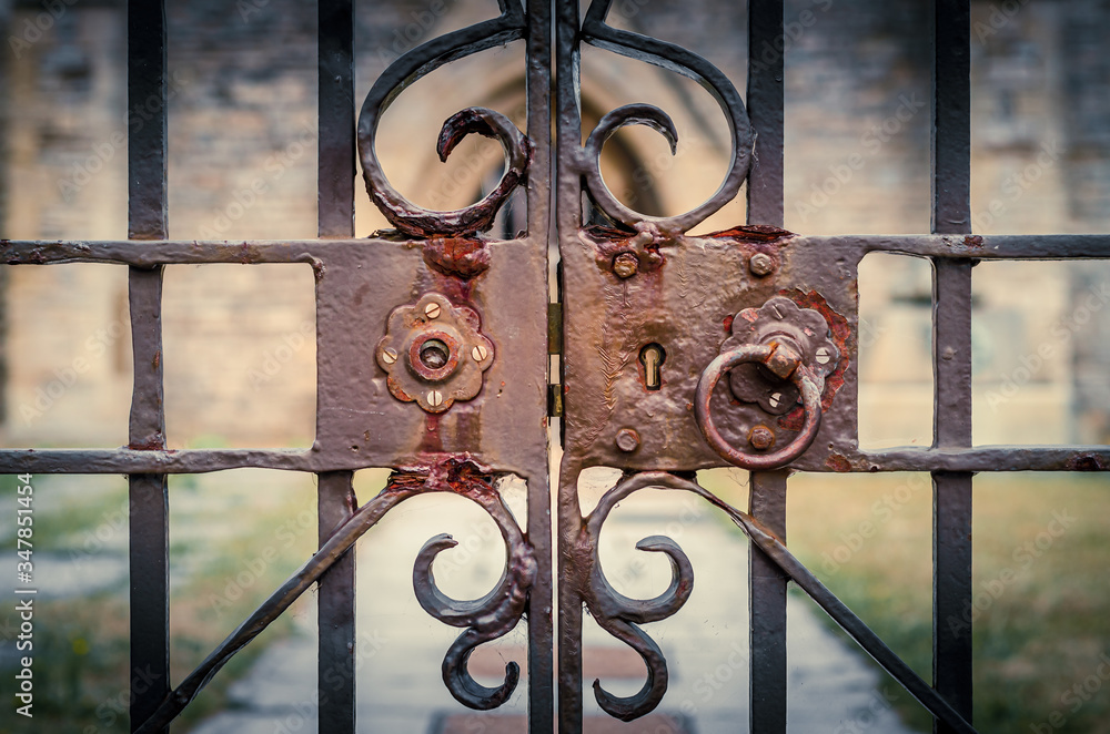 Old and rusty lock on ornate, locked iron gates of a church