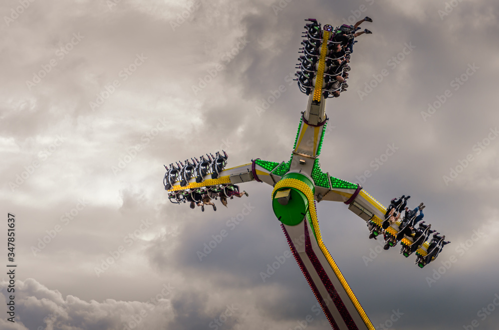 Looking up at thrill seekers on a fairground ride against a dramatic cloudy sky