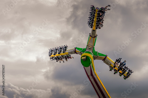 Obraz na płótnie Looking up at thrill seekers on a fairground ride against a dramatic cloudy sky w salonie