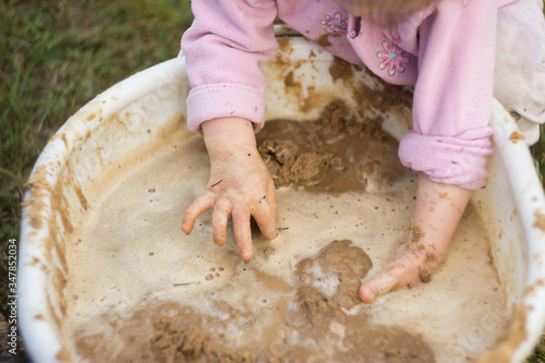 A little girl enthusiastically plays with mud in a basin