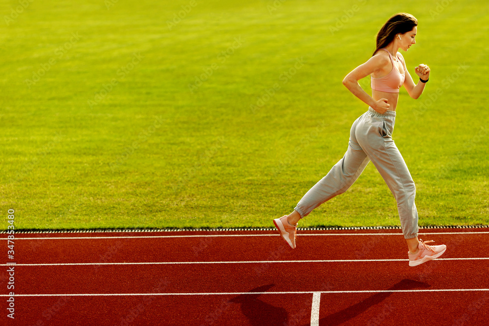 Obraz premium Sporty woman runner on the stadium. Photo of attractive woman in fashionable sportswear. Dynamic movement