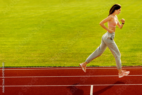 Sporty woman runner on the stadium. Photo of attractive woman in fashionable sportswear. Dynamic movement