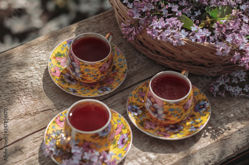 Small cups of tea. Bone china. Yellow and purple. Blooming lilac. Basket with lilac. Lilac and tea on the street. Spring