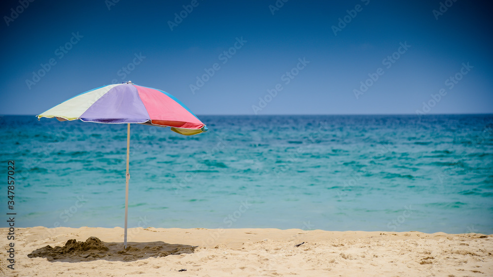 Colourful parasol umbrella on tropical island beach. Holiday relaxation with turquoise sea and blue sky landscape. Summer vacation travel concept