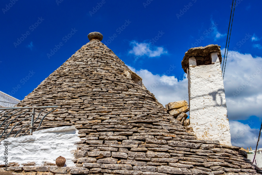 Conical roof with chimney of an old trullo, traditional Apulian dry stone hut in Alberobello, Apulia Region, Metropolitan City of Bari, Italy against beautiful cloudy summer sky