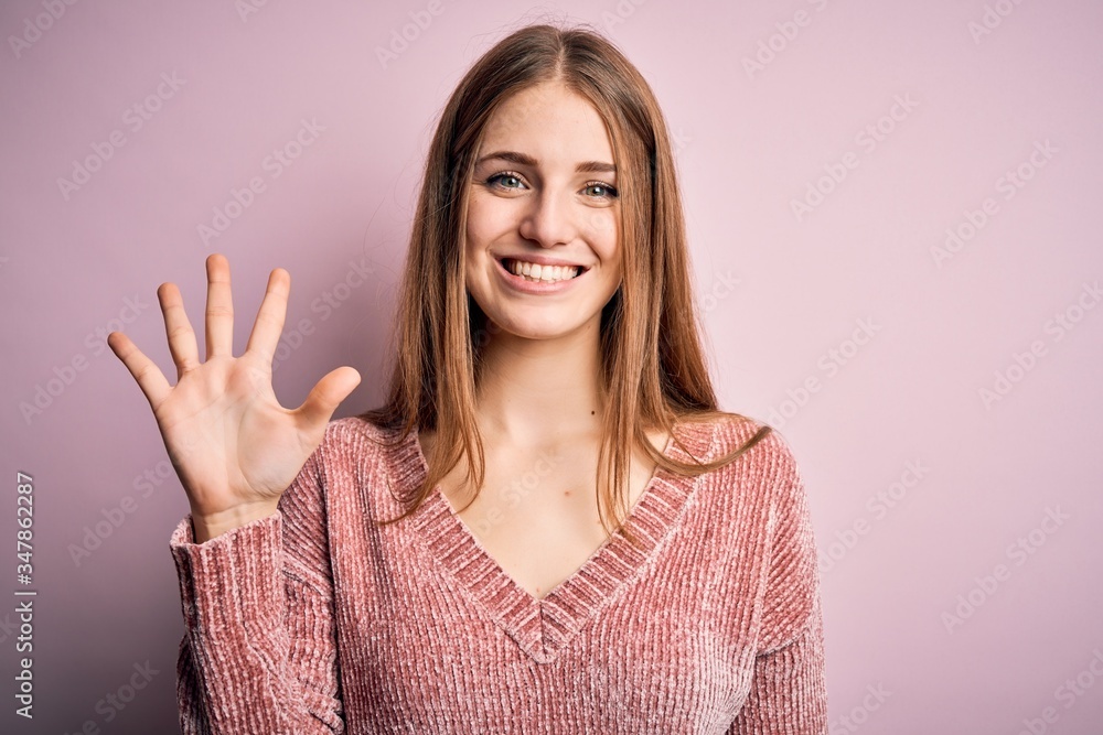 Young beautiful redhead woman wearing casual sweater over isolated pink background showing and pointing up with fingers number five while smiling confident and happy. Young beautiful redhead woman wearing casual sweater over isolated pink background showing and pointing up with fingers number five while smiling confident and happy.