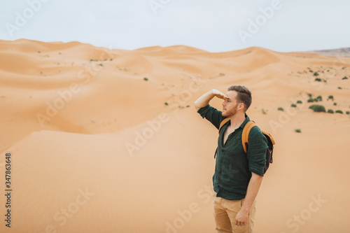 Man backpacker travel in Morocco, Sahara desert. Looking forward and explore african nature, sand dunes around.