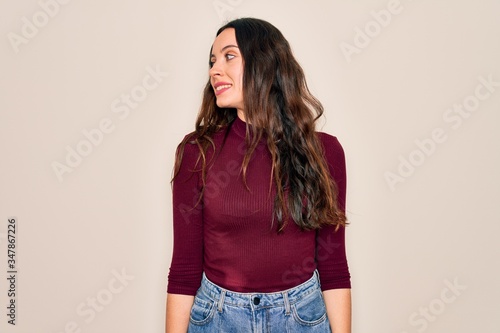 Young beautiful woman wearing casual t-shirt standing over isolated white background looking away to side with smile on face, natural expression. Laughing confident.