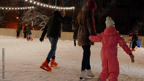 christmas, family and leisure concept - happy mother, father and daughter at outdoor skating rink in winter