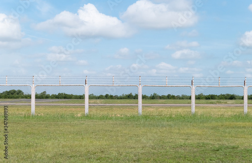 Outdoor background of grass field and fence area with blue sky and white clouds.