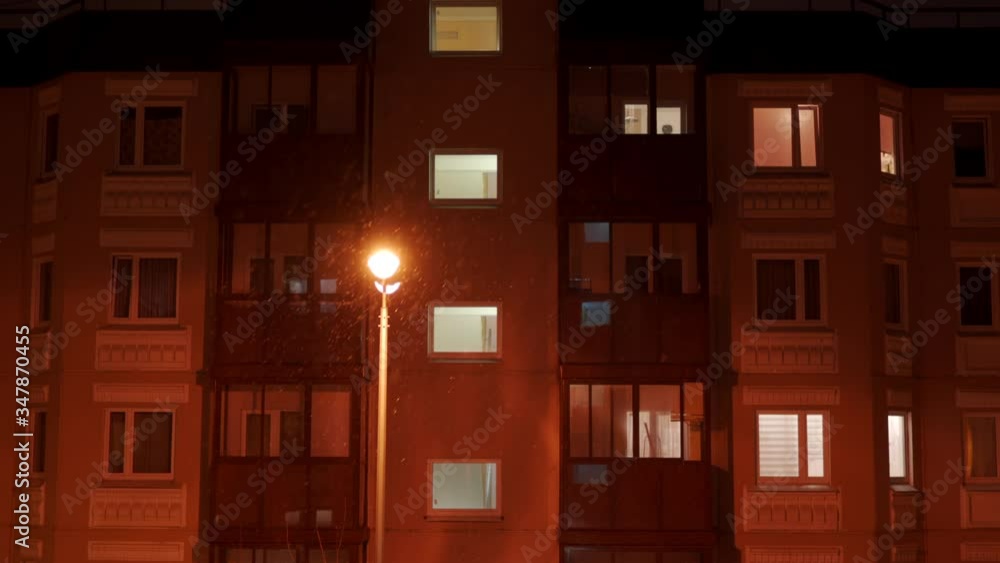 Windows of residential apartment building at dusk in winter, lantern illuminates the falling snow in the yard at night. Windows of residential apartment building at dusk in winter, lantern illuminates the falling snow in the yard at night.