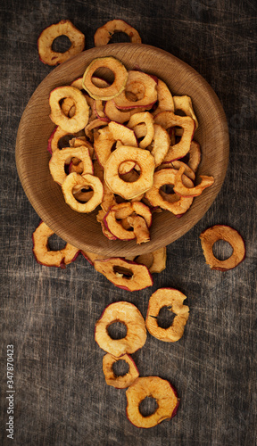 Apple ring chips in a wooden bowl and scattered on dark brown wooden background, table, copy space, top view, vertical