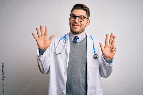 Young doctor man with blue eyes wearing medical coat and stethoscope over isolated background showing and pointing up with fingers number nine while smiling confident and happy. © Krakenimages.com