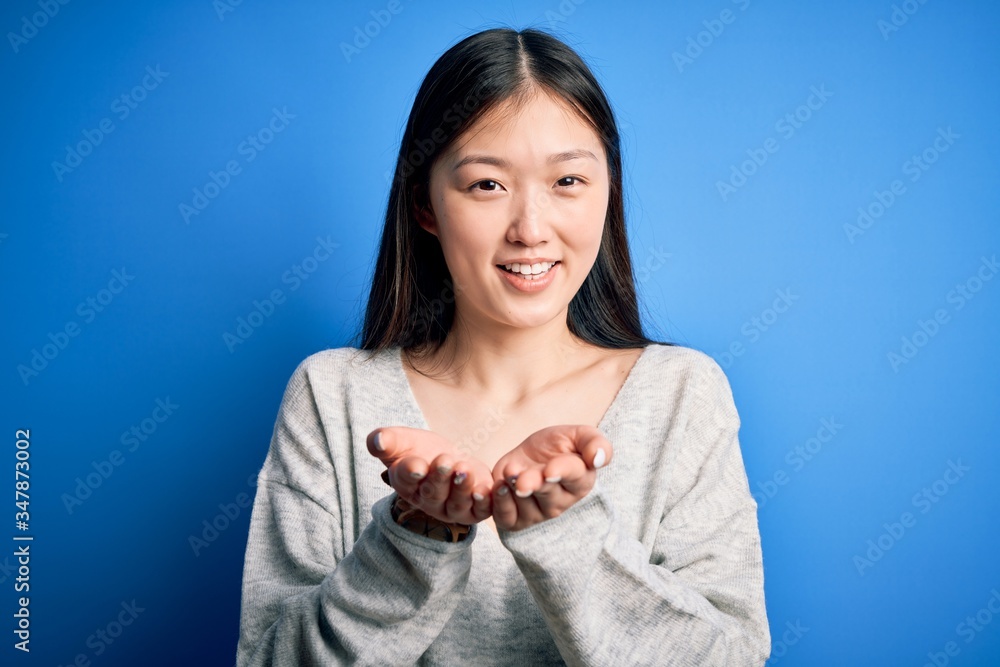 Young beautiful asian woman wearing casual sweater standing over blue isolated background Smiling with hands palms together receiving or giving gesture. Hold and protection Young beautiful asian woman wearing casual sweater standing over blue isolated background Smiling with hands palms together receiving or giving gesture. Hold and protection