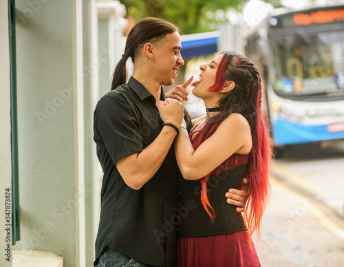 Modern young couple holding each other on the street with blurred background, pretending that they are discussing the relationship, the girl has red hair, and the boy has long hair, Latinos