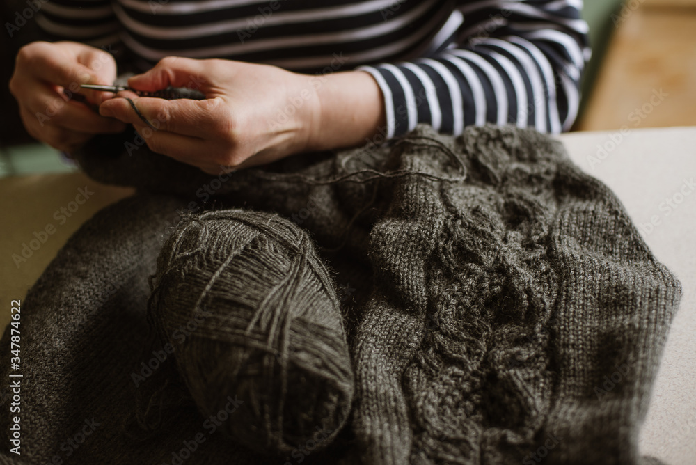 Close up photo of woman's hands knitting on grey yarn on wooden background