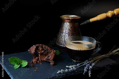 A delicious chocolate muffin, a cup of black coffee, a cezve with custard coffee. Decorated with mint and lavender.