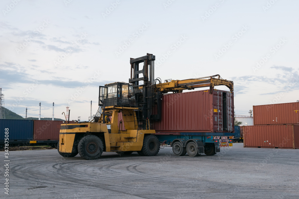 Forklift is loading container box to truck at train station near petrochemical plant in the evening