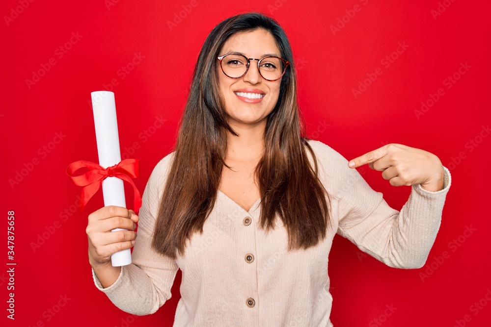 Young hispanic smart woman wearing glasses holding university degree over red background with surprise face pointing finger to himself Young hispanic smart woman wearing glasses holding university degree over red background with surprise face pointing finger to himself