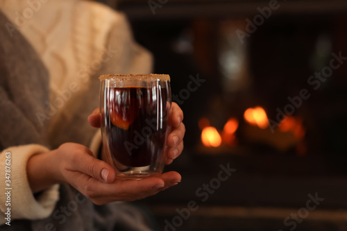 Woman with mulled wine near fireplace indoors, closeup. Winter vacation