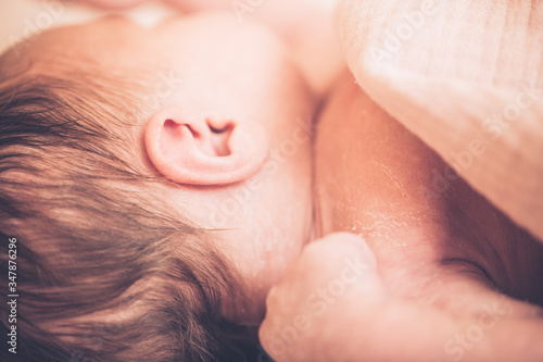 Newborn baby boy lying on bed, sleeping, close up. Healthy newborn baby sleeping, showing close up of ear and side of babies head.