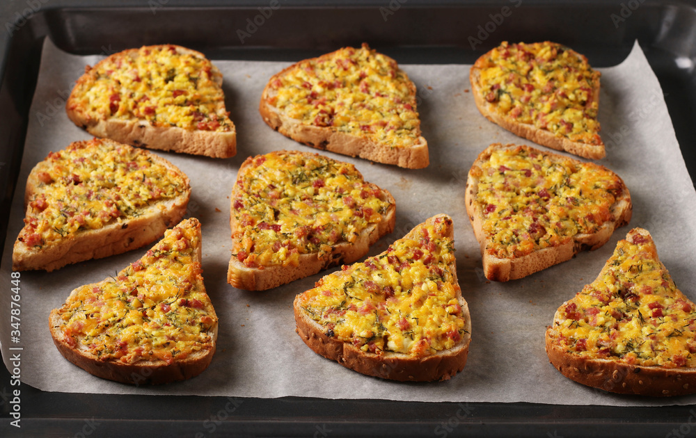 Homemade hot sandwiches with cheese and sausage, on parchment on a baking tray, Horizontal format, closeup Homemade hot sandwiches with cheese and sausage, on parchment on a baking tray, Horizontal format, closeup