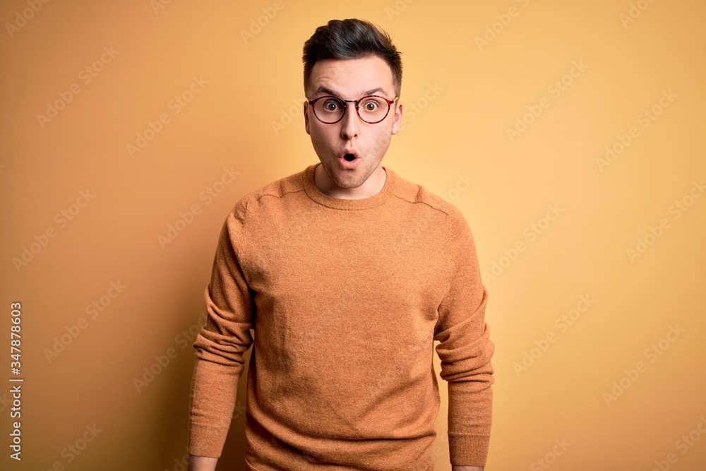 Young handsome caucasian man wearing glasses and casual winter sweater over yellow background afraid and shocked with surprise expression, fear and excited face. Young handsome caucasian man wearing glasses and casual winter sweater over yellow background afraid and shocked with surprise expression, fear and excited face.