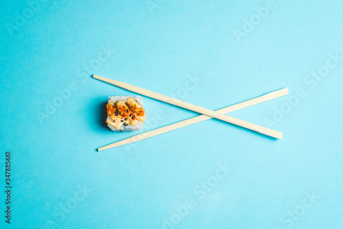 Piece of sushi between two chopsticks on a blue background 