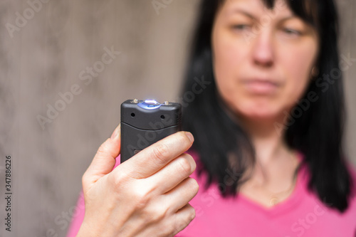 A woman will use a stun gun with a powerful electric discharge. The girl holds a personal taser in her hands to protect against bandits. The female turned on the device for her protection. photo