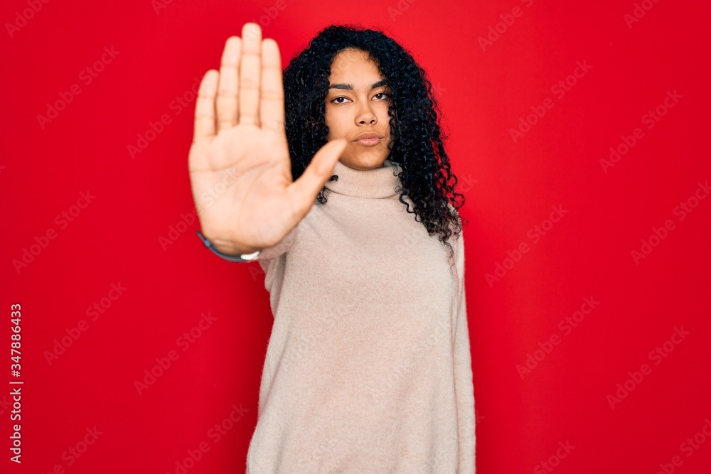 Young african american curly woman wearing casual turtleneck sweater over red background doing stop sing with palm of the hand. Warning expression with negative and serious gesture on the face. Young african american curly woman wearing casual turtleneck sweater over red background doing stop sing with palm of the hand. Warning expression with negative and serious gesture on the face.