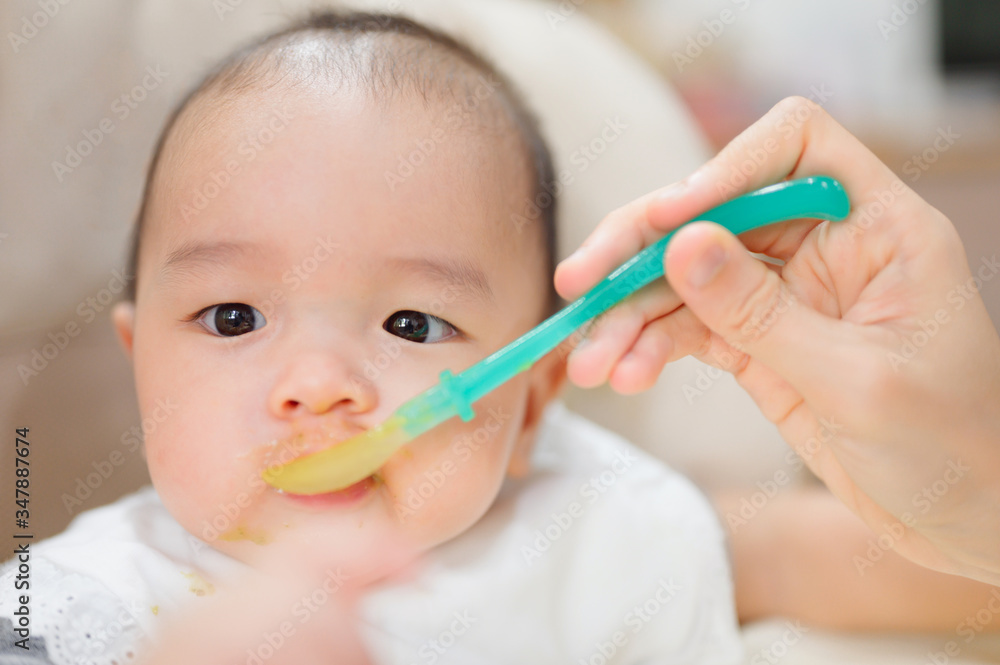 Asian baby boy eating blend food on a high chair, Mother Feeds A Little Baby With A Spoonful Of Food ,eating first time at home Asian baby boy eating blend food on a high chair, Mother Feeds A Little Baby With A Spoonful Of Food ,eating first time at home
