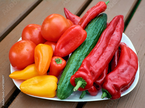 Group of vegetables on a plate close-up. Mix of vegetables. Paprika, tomatoes and cucumber. Wooden table photo