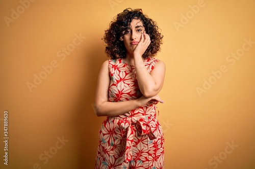 Young beautiful curly arab woman on vacation wearing summer floral dress and sunglasses thinking looking tired and bored with depression problems with crossed arms.