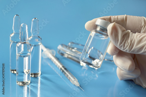 Medical vial of drug in the hands of a medical professional on a light blue background with a glass ampoules and a disposable syringe. Shallow depth of field, selective focus. Healthcare concept. photo