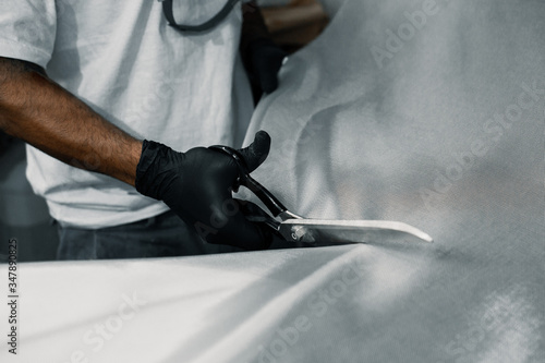 Manufacturing process of a surfboard by a white shirt shaper and black gloves inside his workshop. He uses white foambord, fiberglass cloth and tools to make his board. photo