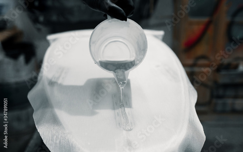 Manufacturing process of a surfboard by a white shirt shaper and black gloves inside his workshop. He uses white foambord, fiberglass cloth and tools to make his board.