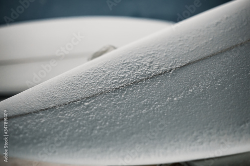 Manufacturing process of a surfboard by a white shirt shaper and black gloves inside his workshop. He uses white foambord, fiberglass cloth and tools to make his board.