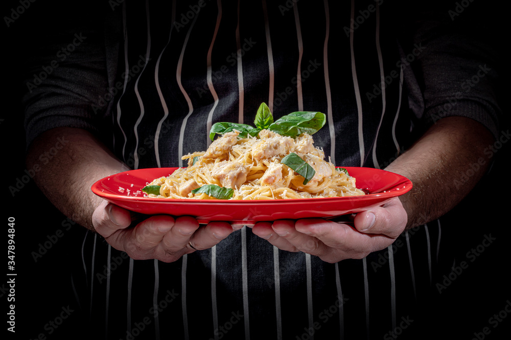 Man holding tasty appetizing classic italian spaghetti pasta with chicken on a dark background
