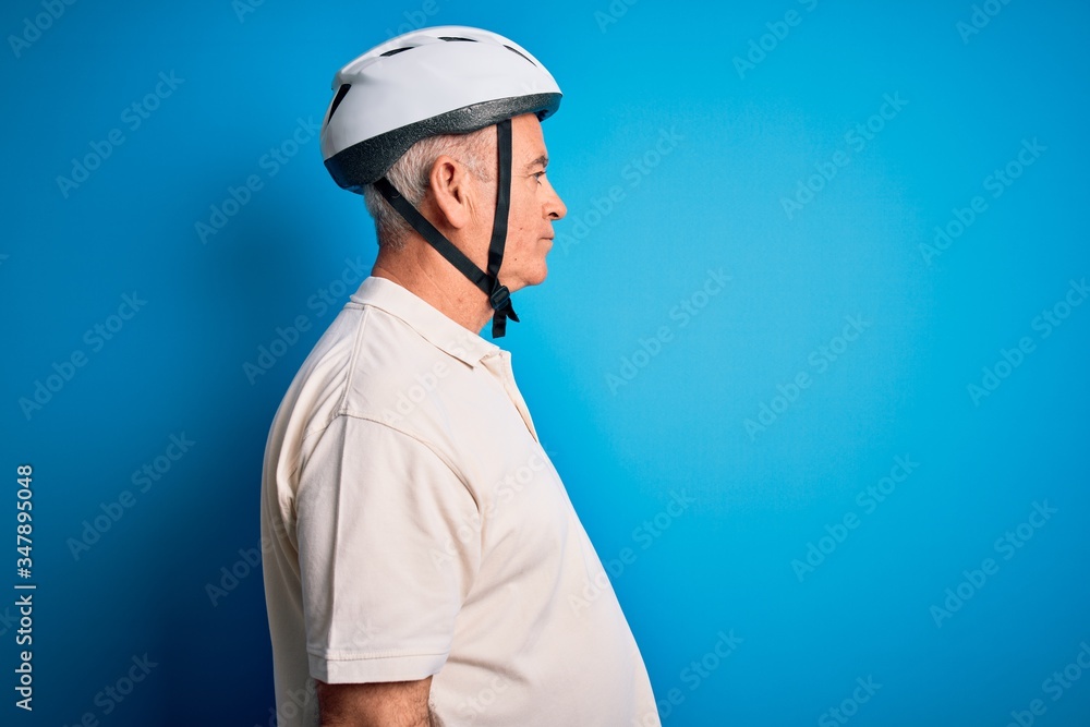 Middle age hoary cyclist man wearing bike security helmet over isolated blue background looking to side, relax profile pose with natural face with confident smile. Middle age hoary cyclist man wearing bike security helmet over isolated blue background looking to side, relax profile pose with natural face with confident smile.