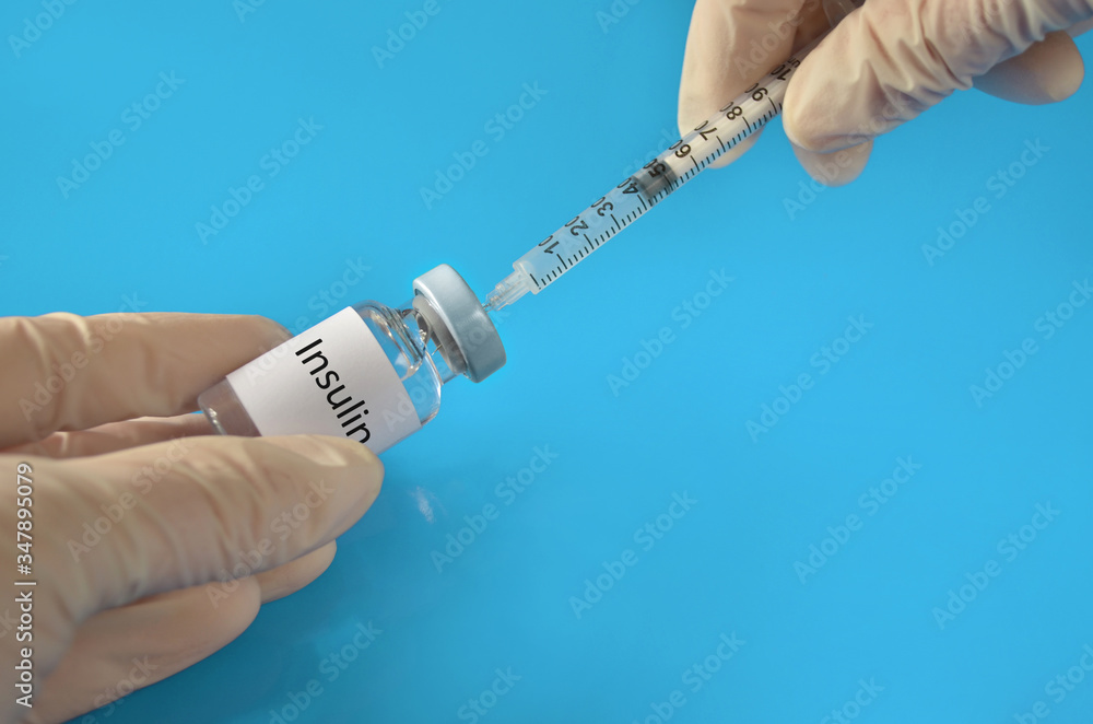 Filling insulin to syringe before inject. Medical vial with a insulin and a disposable syringe in the hands of a medical professional on a blue background. Healthcare concept. Filling insulin to syringe before inject. Medical vial with a insulin and a disposable syringe in the hands of a medical professional on a blue background. Healthcare concept.