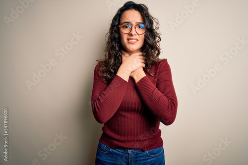 Beautiful woman with curly hair wearing casual sweater and glasses over white background shouting and suffocate because painful strangle. Health problem. Asphyxiate and suicide concept.